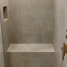 Eine moderne Dusche mit glatten, grauen Wänden und einem eleganten goldenen Bedienfeld für die Wassersteuerung.