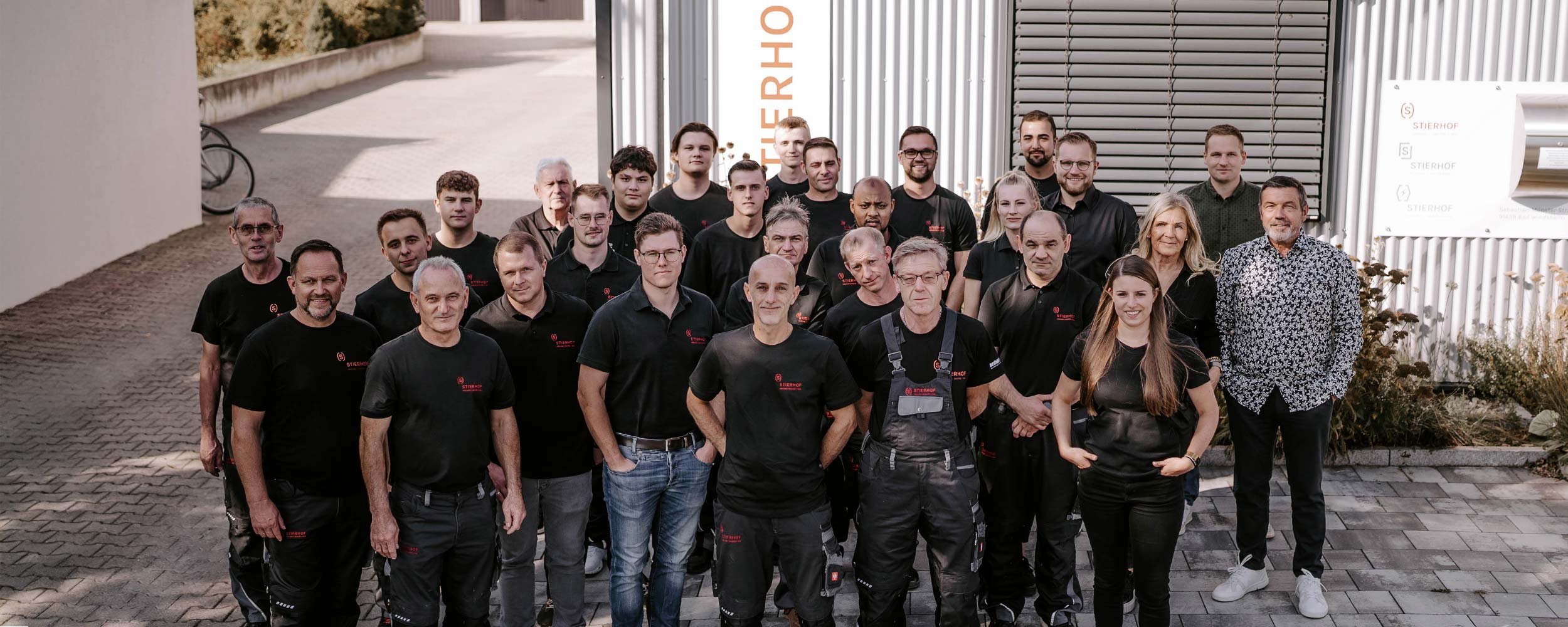 Mitarbeiter eines Unternehmens posieren gemeinsam im Freien, umgeben von einer urbanen Kulisse und einem Fahrrad im Hintergrund.