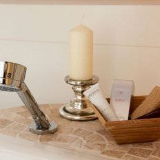 Auf einem Marmorwaschtisch sind ein moderner Wasserhahn, eine Kerze und verschiedene Kosmetikartikel in einem Holzbehälter angeordnet.