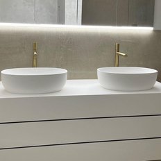 Zwei elegante, weiße Waschbecken auf einem modernen, minimalistischen Unterschrank mit goldenen Wasserhähnen.