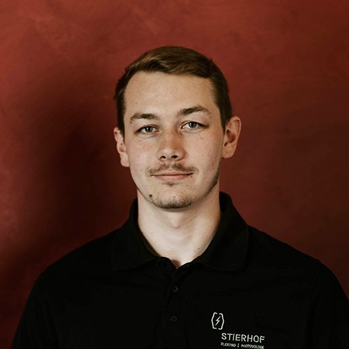 Ein junger Mann mit kurzem, braunem Haar trägt ein schwarzes Polohemd und schaut direkt in die Kamera.