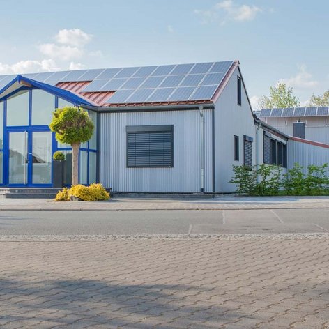 Das Gebäude zeigt eine Kombination aus modernen architektonischen Elementen und umweltfreundlichen Solarpanelen auf dem Dach.