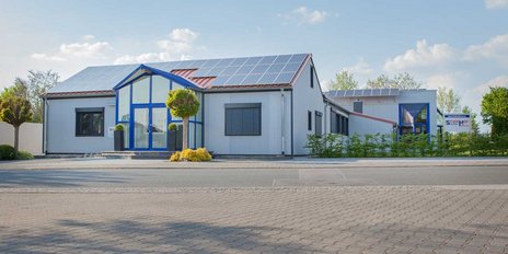 Das Gebäude zeigt eine Kombination aus modernen architektonischen Elementen und umweltfreundlichen Solarpanelen auf dem Dach.