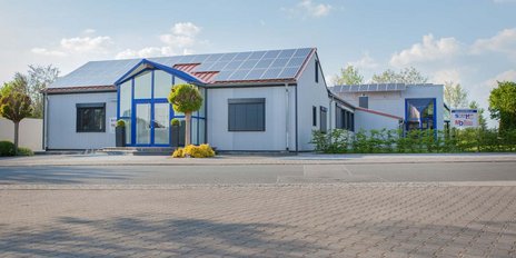 Das Gebäude zeigt eine Kombination aus modernen architektonischen Elementen und umweltfreundlichen Solarpanelen auf dem Dach.