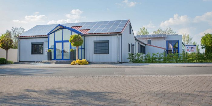 Das Gebäude zeigt eine Kombination aus modernen architektonischen Elementen und umweltfreundlichen Solarpanelen auf dem Dach.