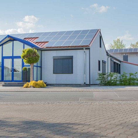 Das Gebäude zeigt eine Kombination aus modernen architektonischen Elementen und umweltfreundlichen Solarpanelen auf dem Dach.