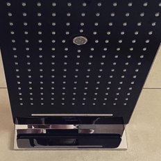 Ein eleganter, schwarzer Duschkopf mit vielen kleinen Düsen, der auf einem modernen Badezimmerboden steht.