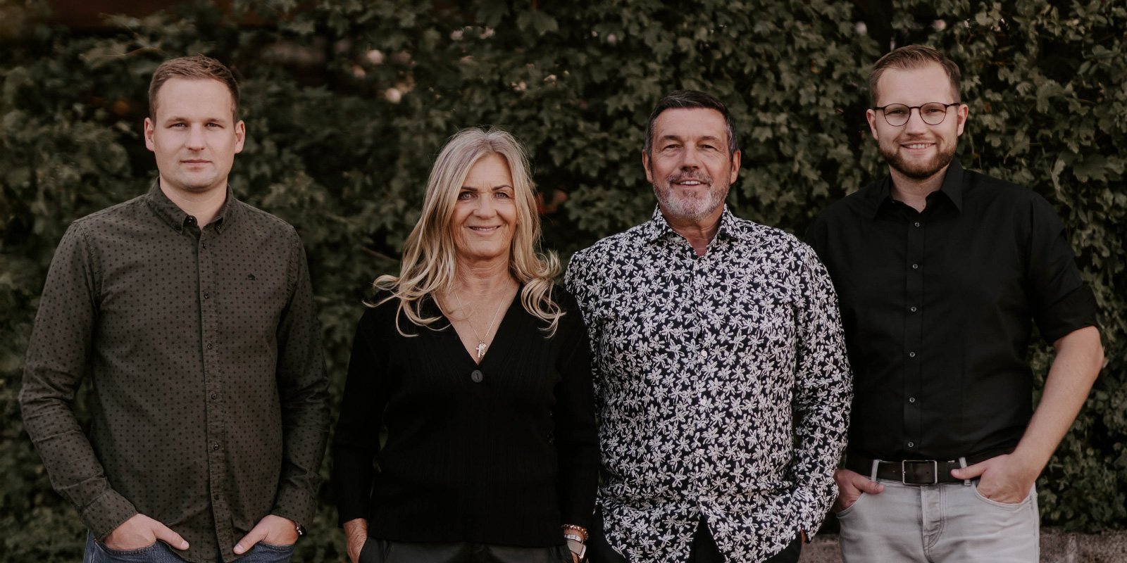 Eine Gruppe von vier Erwachsenen posiert entspannt im Freien, umgeben von üppigem Grün, jeder mit einem individuellen Stil.