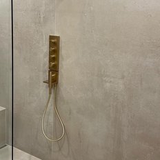 Die Dusche zeigt eine stilvolle goldene Duschsteuerung an einer glatten, grauen Wand, die ein modernes Ambiente schafft.