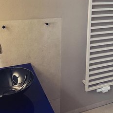 Ein elegantes, schwarzes Waschbecken steht auf einer blauen Oberfläche, daneben ein goldener Wasserhahn und ein Heizkörper.