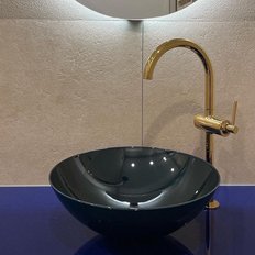 Ein stilvolles, schwarzes Waschbecken mit einem goldenen Wasserhahn, umgeben von einer hellen, strukturierten Wand und blauer Arbeitsplatte.