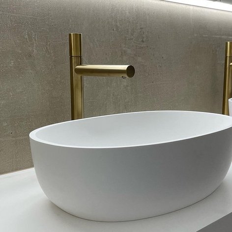 Ein stilvolles, weißes Waschbecken mit einem goldenen Wasserhahn vor einer schlichten, grauen Wand.