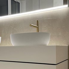 Zwei elegante, weiße Waschbecken mit goldenen Wasserhähnen stehen auf einem modernen, minimalistischen Unterschrank.