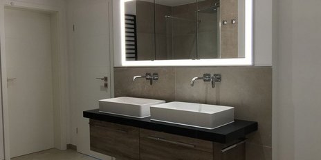 Der stilvolle Raum zeigt eine elegante Kombination aus Holz und Stein, mit einem großen Spiegel und zwei Wasserhähnen.