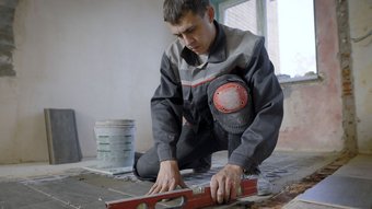 Ein Fliesenleger der mit einer Wasserwaage die Fliesen ausrichtet